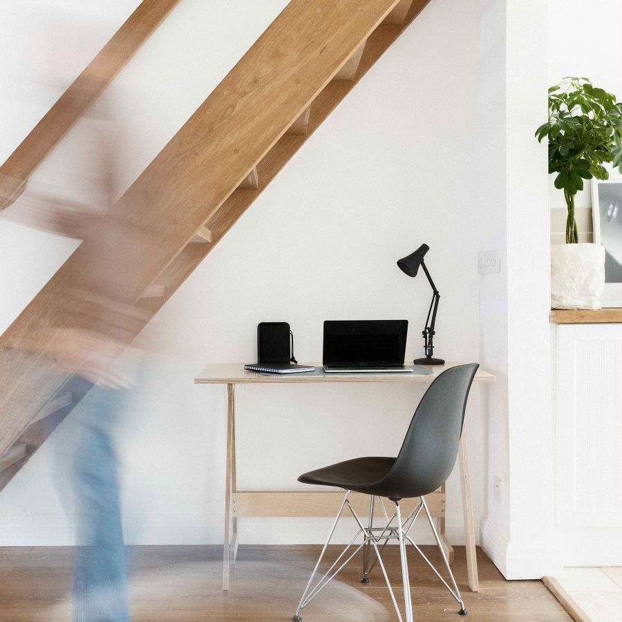Minimalistisches Homeoffice unter einer Holztreppe mit Laptop, Lampe und Stuhl, kombiniert mit natürlichem und modernem Design.