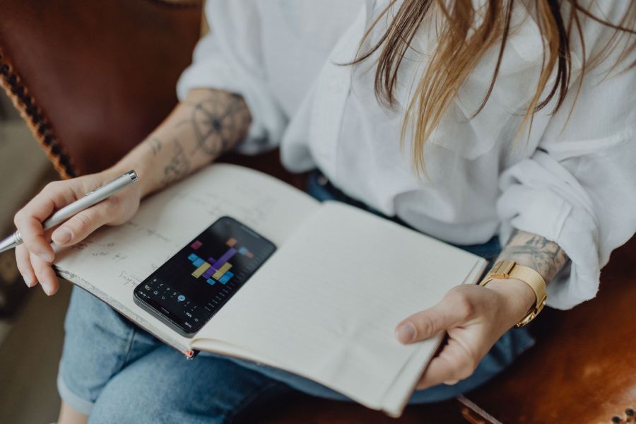 Person mit Notizbuch und Smartphone, plant Aufgaben mit einer App, Fokus auf Organisation und Produktivität im modernen Stil.