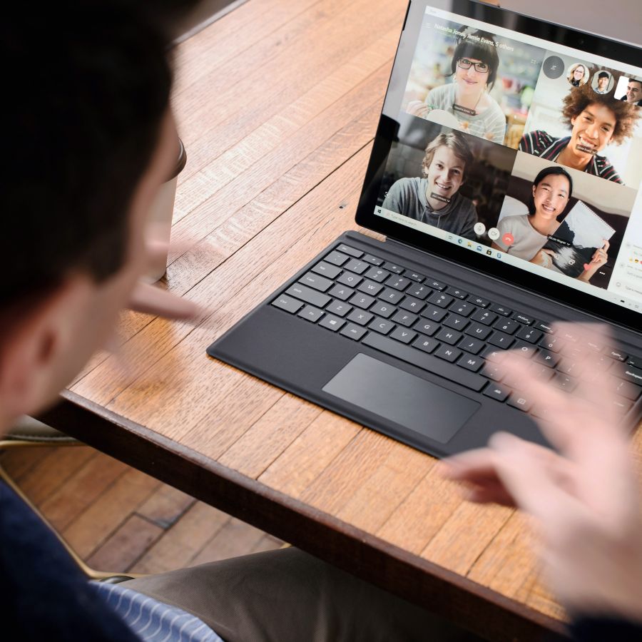 Person nimmt an einer Videokonferenz auf einem Laptop teil, mit mehreren Teilnehmern auf dem Bildschirm, modernes Remote-Meeting.