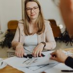 Geschäftsfrau im Gespräch mit Skizzen und Markern am Holztisch, Fokus auf kreative Zusammenarbeit und professionellen Austausch.