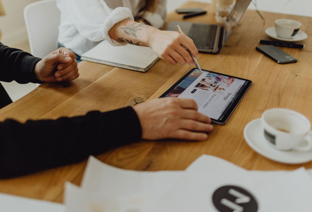 Teamarbeit am Holztisch mit Tablet und Laptop, Fokus auf Diskussion und Planung, unterstützt durch digitale Tools und Notizen.